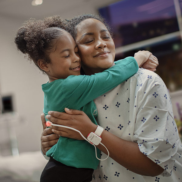 Mother embracing her child in a hospital setting while a Masimo sensor tracks her oxygen levels.